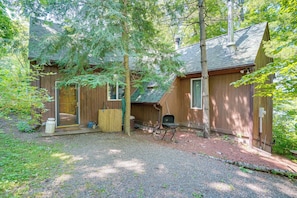 A wooden cabin with a gravel driveway, a wooden deck, and a covered outdoor seating area.