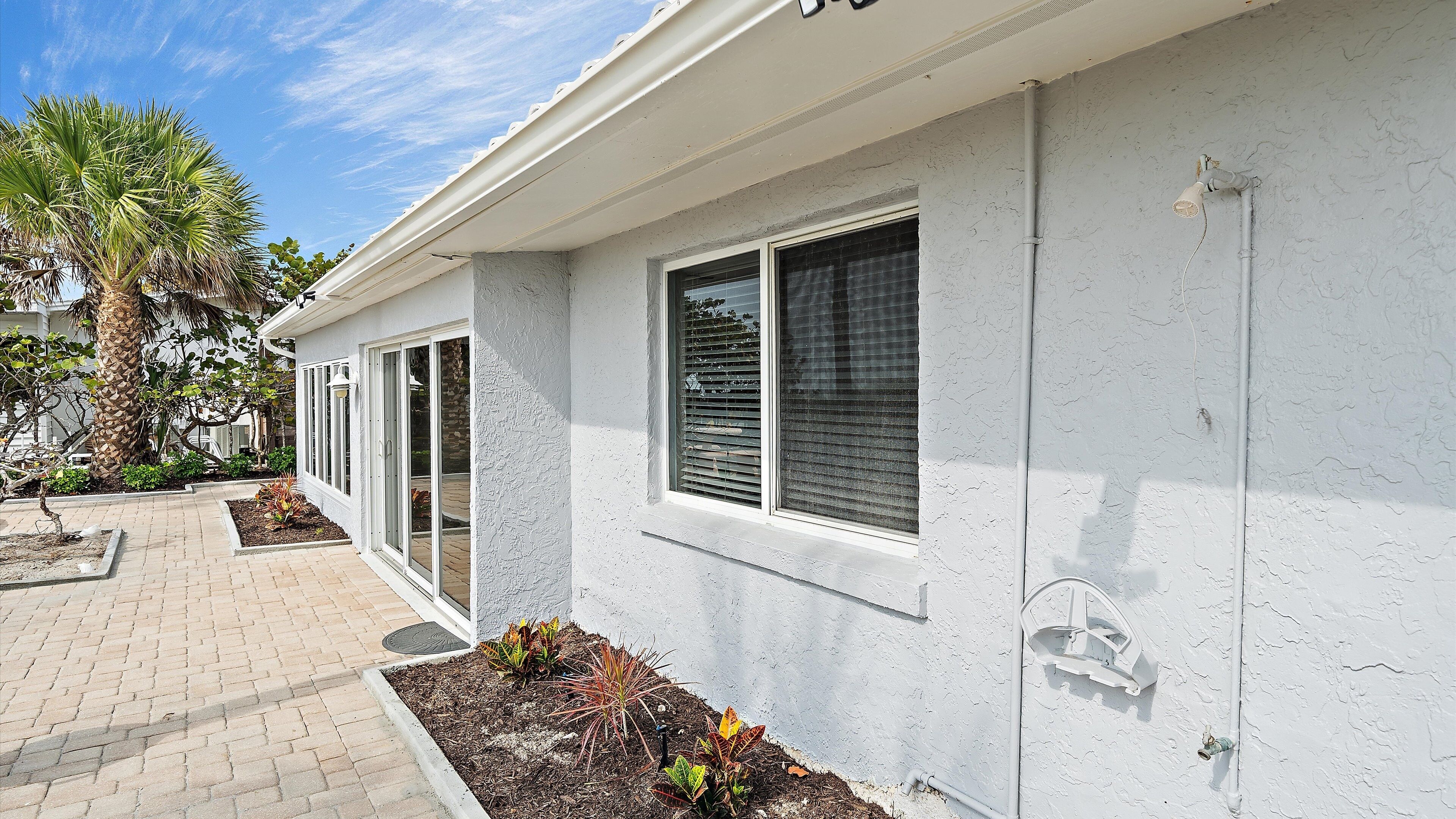 A building with white exterior walls, large windows with blinds, and a paved walkway.