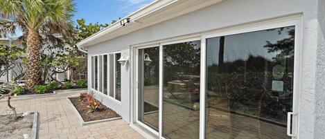 A modern house with large sliding glass doors, a brick pathway, and a palm tree.