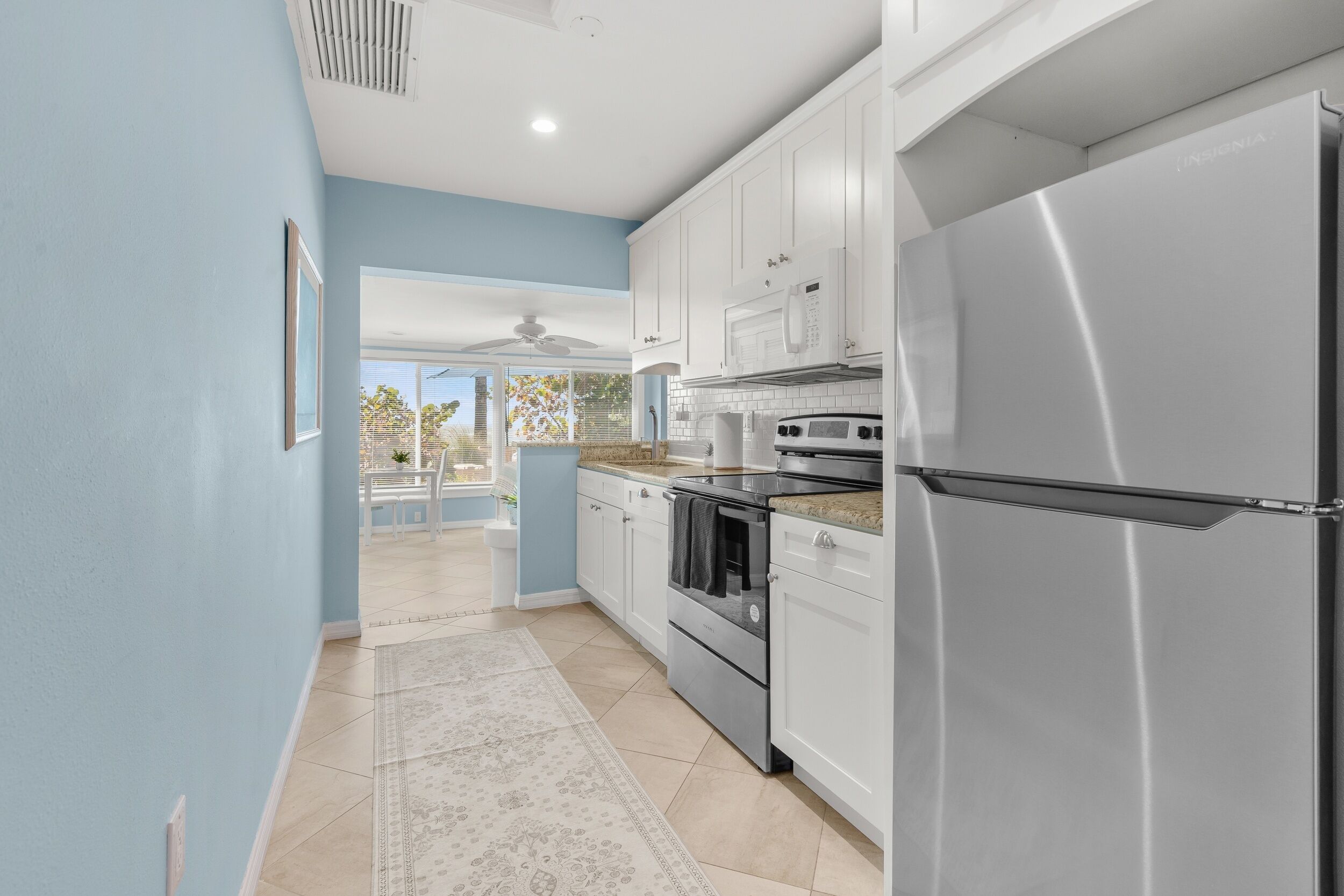 A modern kitchen with white cabinets, stainless steel appliances, and a view to the outside.