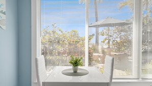 A dining table with a potted plant, white chairs, and a window with blinds. - Las Hermanas 4 1 Bedroom Studio by RedAwning (Longboat Key)