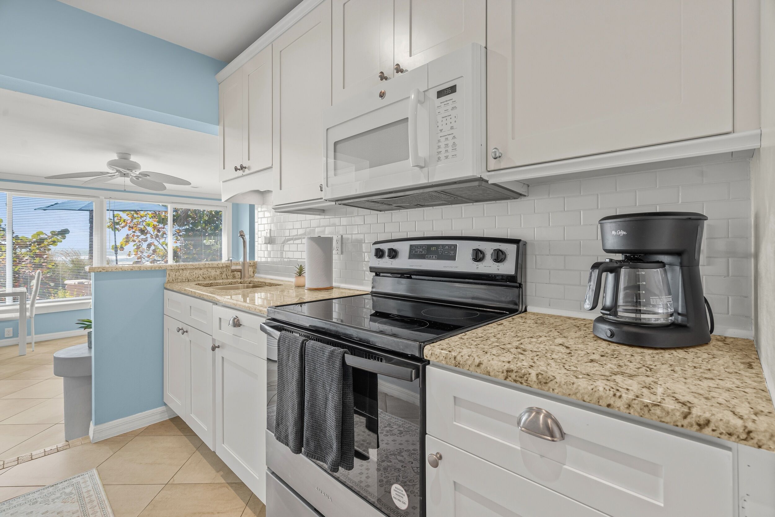 A modern kitchen with white cabinets, a black stove, a microwave, and a coffee maker.