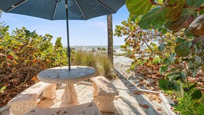 An outdoor patio with a stone table and bench, surrounded by foliage and a view of the beach. - Las Hermanas 4 1 Bedroom Studio by RedAwning (Longboat Key)