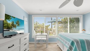 A bedroom with a large window, a bed, a TV on a dresser, and a ceiling fan. - Las Hermanas 4 1 Bedroom Studio by RedAwning (Longboat Key)