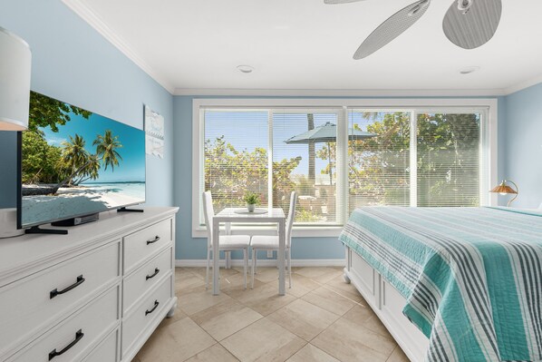 A bedroom with a large window, a bed, a TV on a dresser, and a ceiling fan.