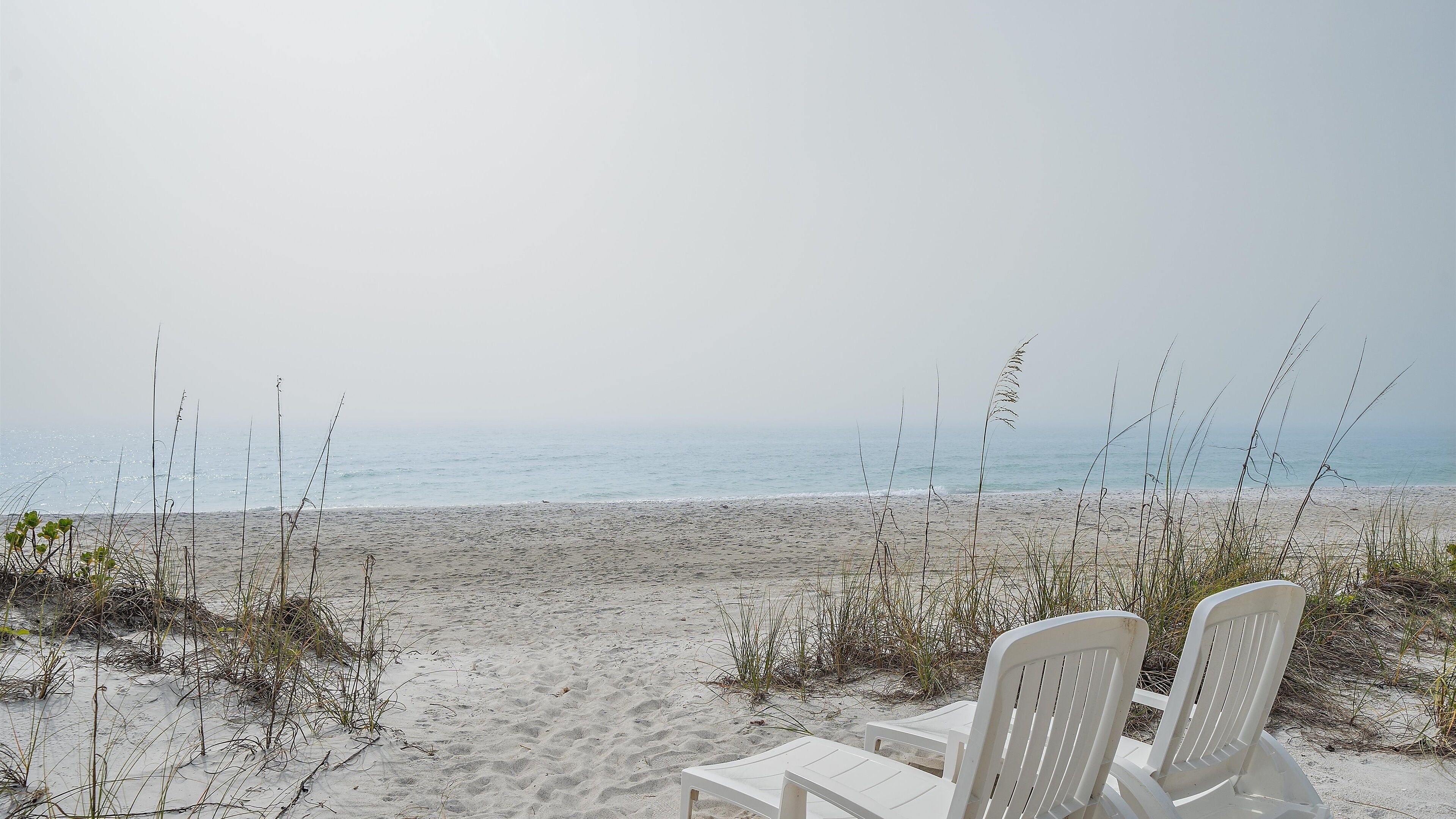 A beach view with two white chairs facing the ocean.