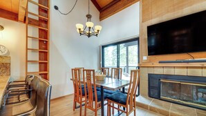 Un coin repas avec une table et des chaises en bois, un lustre, une cheminée et un téléviseur fixé au-dessus.