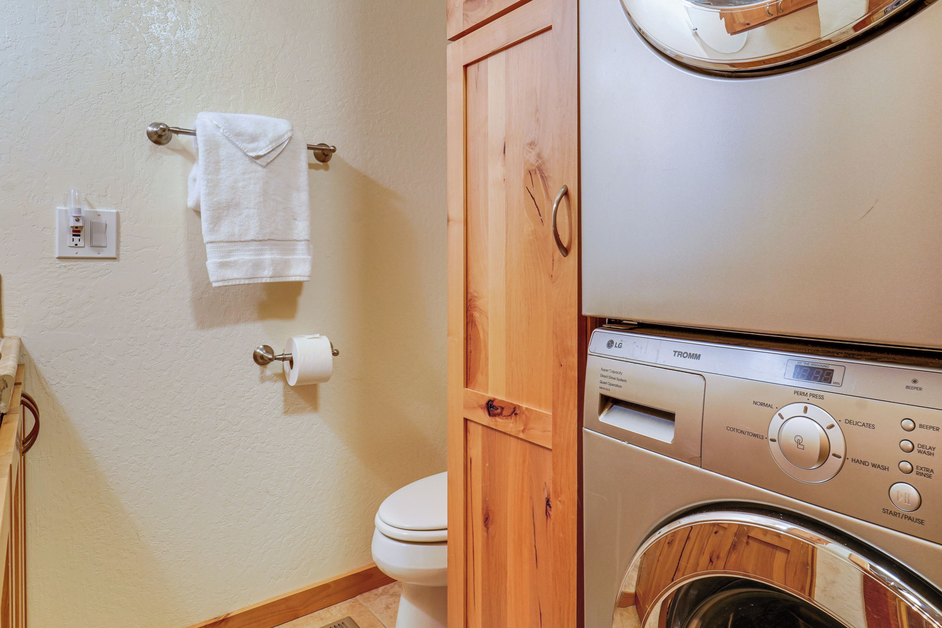 A laundry area with a washing machine and dryer, a toilet, and a towel rack with towels.