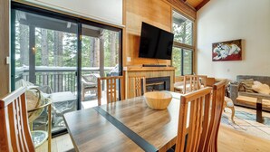 Un salon moderne avec une table à manger en bois, des chaises, un téléviseur à écran plat fixé au mur et une cheminée.