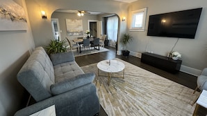 A modern living room with a grey sofa, a marble coffee table, and a flat-screen TV mounted on the wall. - Spacious Retreat Near Convention Centers 4 Bedroom Home by RedAwning (Des Plaines)