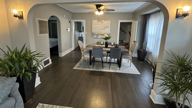 A modern living room with a dining area, dark wood flooring, and a ceiling fan. - Spacious Retreat Near Convention Centers 4 Bedroom Home by RedAwning (Des Plaines)