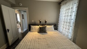 A bedroom with a bed, a nightstand, a wall-mounted light, and a door leading to another room. - Spacious Retreat Near Convention Centers 4 Bedroom Home by RedAwning (Des Plaines)