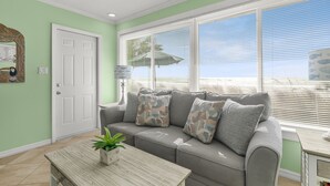 A living room with a grey sofa, patterned cushions, a wooden coffee table with a plant, and a large window with blinds. - Las Hermanas 1 Studio by RedAwning (Longboat Key)