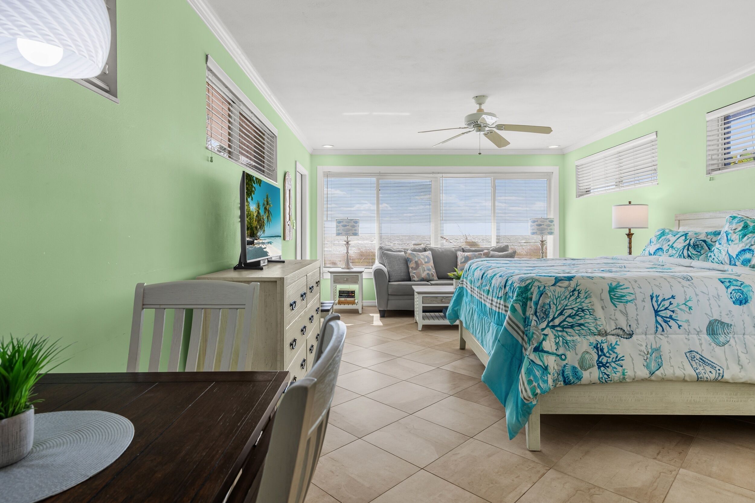 A room with a bed, a desk, a chair, a dining table, and a window with blinds.