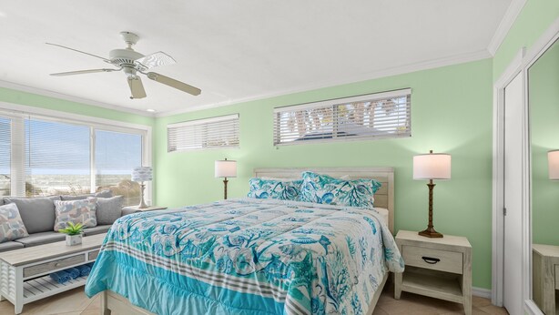 A bedroom with a bed, two bedside tables, a ceiling fan, and a window with blinds. - Las Hermanas 1 Studio by RedAwning (Longboat Key)