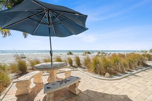 A stone table with a mosaic top, an umbrella, and a bench on a paved walkway by the beach. - Las Hermanas 1 Studio by RedAwning (Longboat Key)