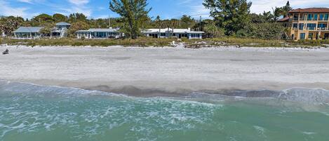 Une propriété située en bord de mer, avec une plage de sable, un ciel bleu dégagé et quelques bâtiments en arrière-plan.
