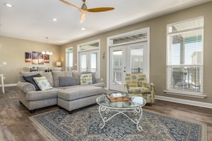 A living room with a sectional sofa, a glass coffee table, and a patterned rug.