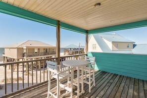 A wooden deck with a table and chairs, overlooking a beach with buildings in the background. - Lazy Daze Beach House - 105 Strand Ct 3 Bedroom Home by RedAwning (Dauphin Island)