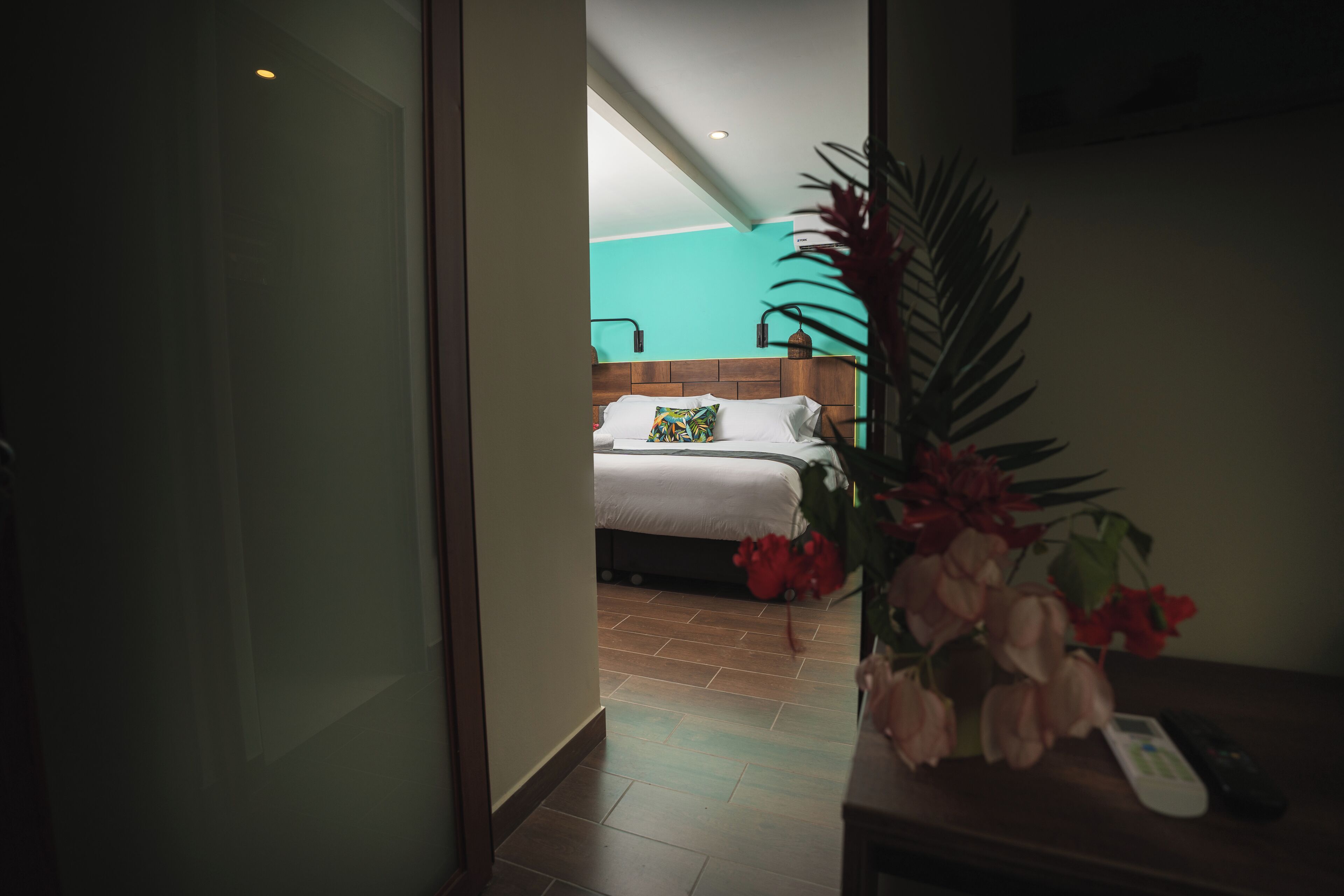 Habitación de hotel con cama, mesita de noche, control remoto y un jarrón con flores.