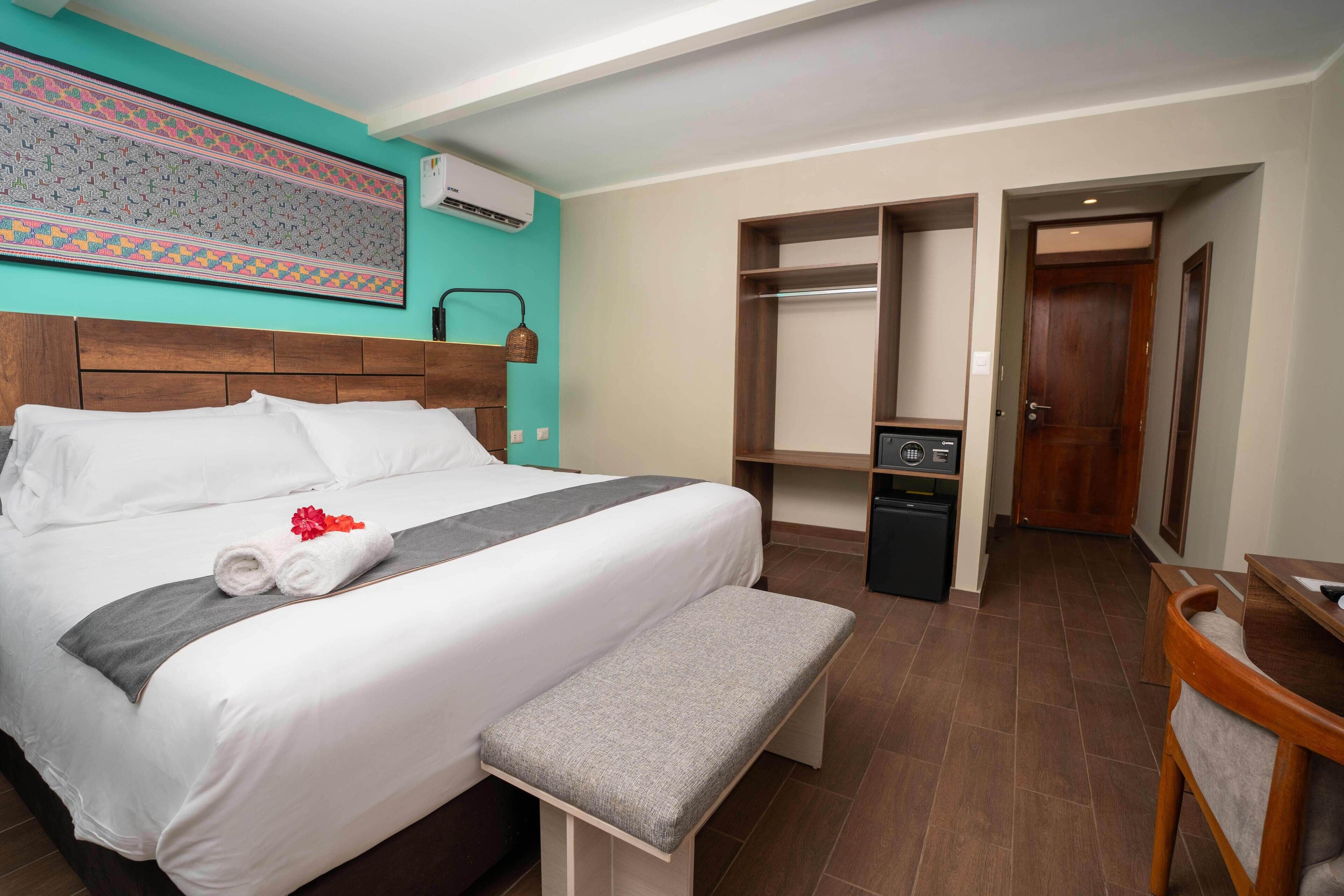 Una habitación de hotel con cama, banco, armario y escritorio.