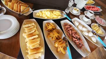 A buffet table with various food items including bread, eggs, ham, and fruits.