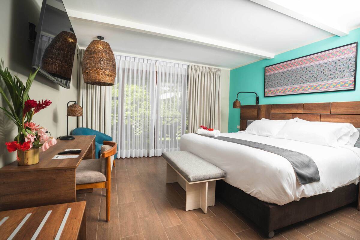 A modern hotel room with a large bed, a desk with a chair, a bench, and a TV mounted on the wall.