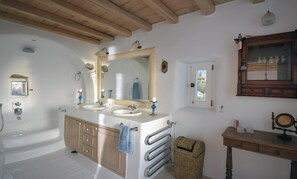 A bathroom with two sinks, a large mirror, wooden cabinets, a towel rack, a wicker basket, and a wooden vanity with a mirror.