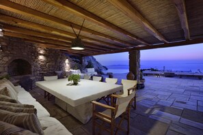 An outdoor dining area with stone walls, a stone fireplace, and a view of the sea.