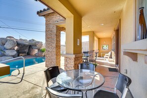 An outdoor patio with a pool, stone pillars, and a glass table with chairs.