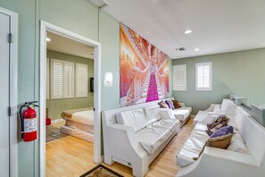 A modern hotel room with a white sofa, a large mural, and a fire extinguisher on the wall.