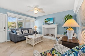 A living room with a grey sofa, white coffee table, wicker chairs, a fireplace, and a ceiling fan. - Las Hermanas 2 1 Bedroom Condo by RedAwning (Longboat Key)