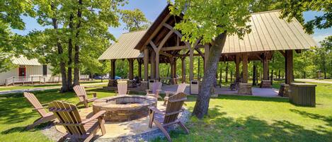 A covered outdoor seating area with Adirondack chairs and a fire pit, surrounded by trees.