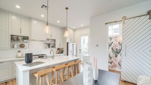 Une cuisine moderne avec des meubles blancs, des tabourets en bois, un îlot central et des luminaires suspendus.