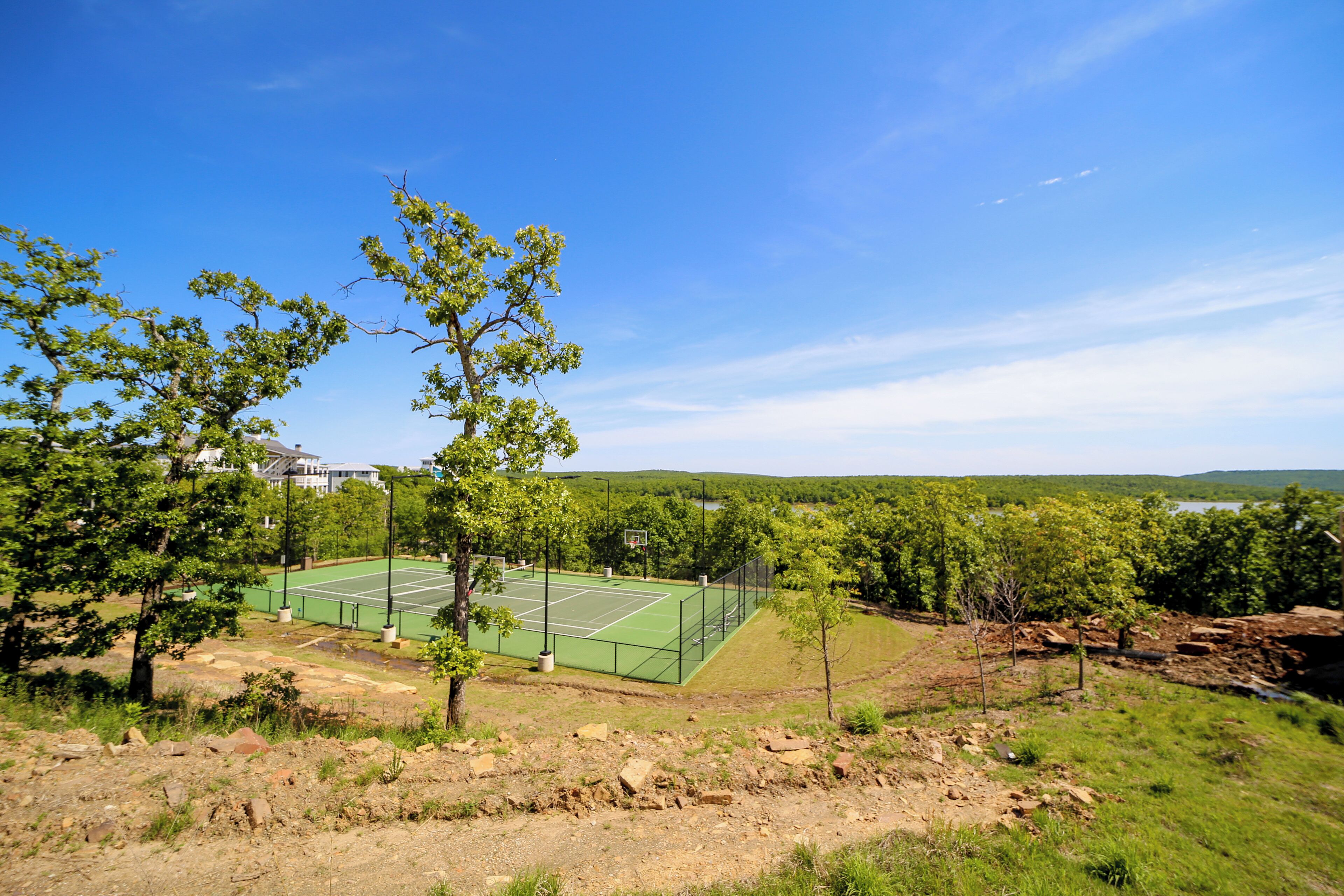 A tennis court surrounded by trees and a hilly landscape.