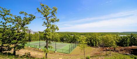 A tennis court surrounded by trees and a hilly landscape.
