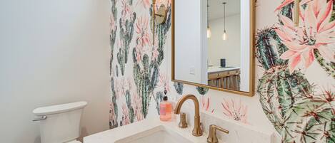 A bathroom with a toilet, sink, and mirror. The walls are decorated with floral wallpaper.