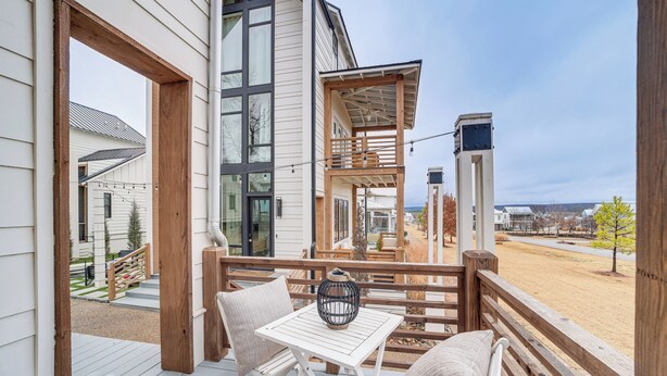 Une terrasse en bois avec une table blanche et deux chaises, donnant sur un quartier résidentiel avec des maisons et un ciel dégagé.