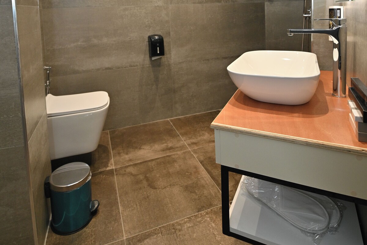 A modern bathroom with a large vessel sink, a toilet, and a shower area.