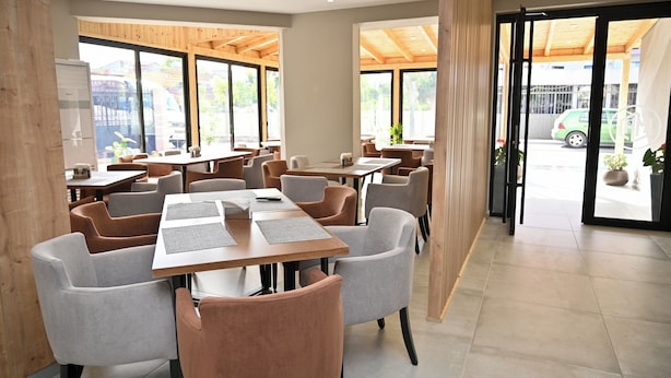 A modern dining area with tables and chairs, large windows, and a view of the street outside. - MondurO Hotel (Durrës)