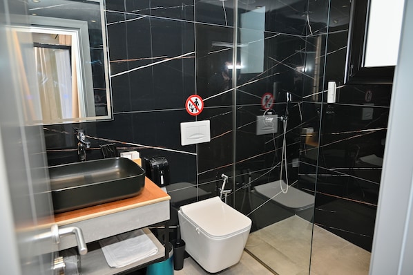 A modern bathroom with a black marble backsplash, a sink with a wooden countertop, a toilet, and a glass shower enclosure. - MondurO Hotel (Durrës)