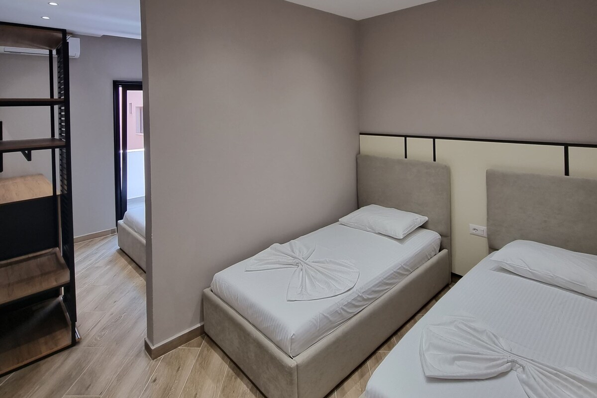 A hotel room with two beds, a wooden bench, and a view of the outside.