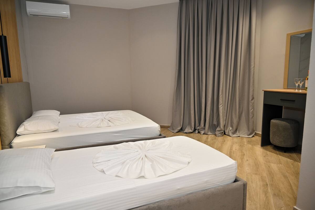A hotel room with two beds, a desk, a mirror, and a window with curtains.