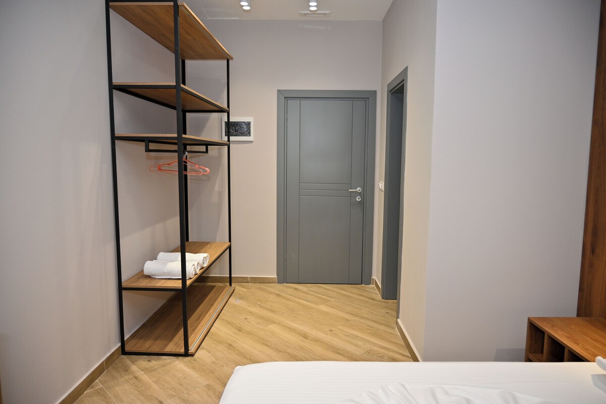 A bedroom with a bed, a wooden wardrobe, a grey door, and a small wooden table.