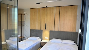 A modern hotel room with two beds, a wooden panel wall, and a glass partition. - MondurO Hotel (Durrës)