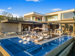 A modern pool area with lounge chairs and umbrellas, a fire pit, and a bar area. - Collingwood - Modern Architectural Home with Spectacular Views (Los Angeles)