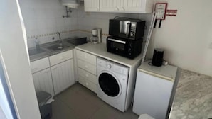 A compact kitchen with a washing machine, a microwave, and a coffee maker. - 1-bed - Sleeps 4 - Free Parking (Portimão)