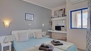 A bedroom with a bed, bedside table, wall-mounted TV, and a window with curtains. - 1-bed - Sleeps 4 - Free Parking (Portimão)
