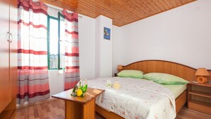 Une chambre avec un plafond en bois, un lit recouvert d’une couette verte et blanche, une petite table sur laquelle se trouvent un citron et des feuilles vertes, et une fenêtre ornée de rideaux à rayures.
