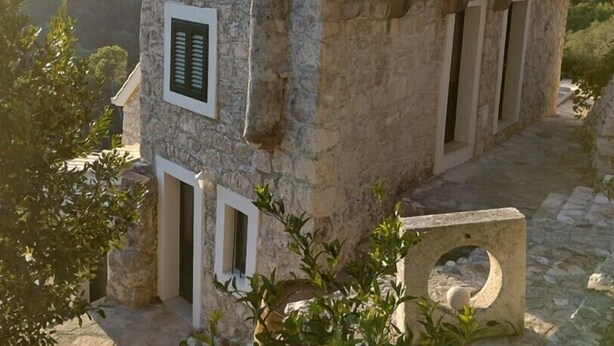 Un bâtiment en pierre avec un toit en tuiles, une petite fenêtre avec des volets et une porte d’entrée.